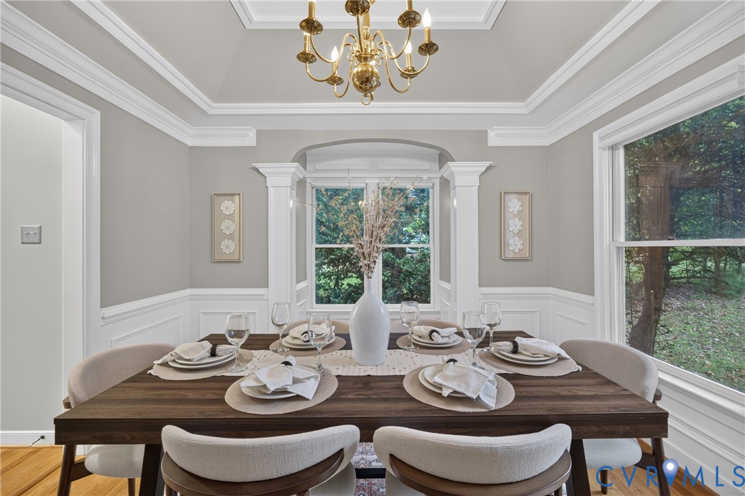 Tray ceiling with crown molding, wainscoting, and a multi-arm brass chandelier