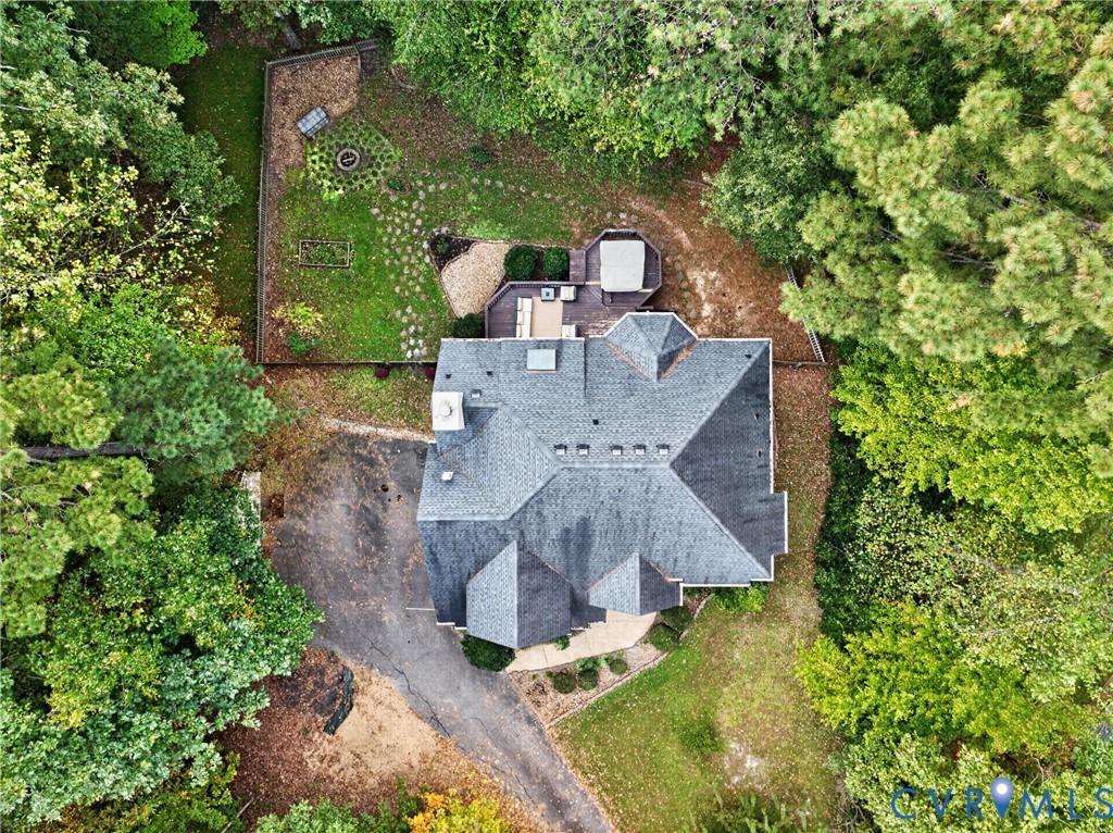 Aerial perspective of a multi-gabled roofline with a chimney, featuring an expansive wooded lot, a multi-level deck, and a stone-paver walkway
