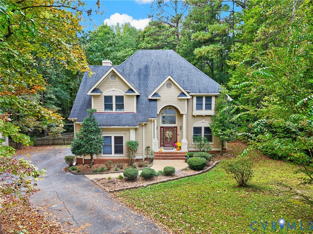 Two-story residence featuring light-toned siding, a steep roofline, multi-pane windows, a brick-accented entryway, and a paved driveway