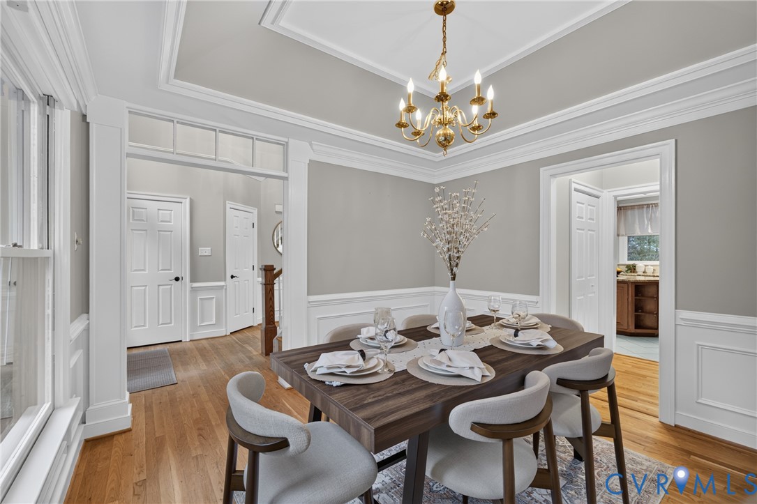 Dining area featuring wood-finish flooring, crisp white wainscoting, a tray ceiling, and a traditional brass chandelier