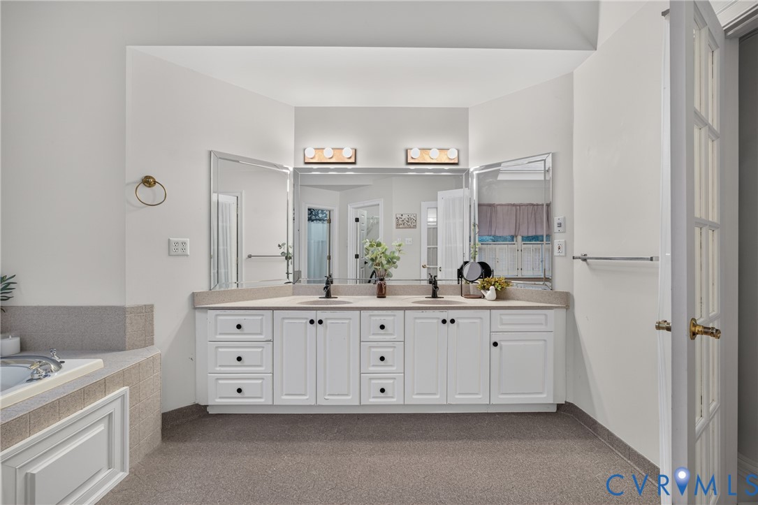 Double vanity featuring white cabinetry, neutral-toned solid surface countertops, dual undermount sinks, and expansive multi-panel mirrors with integrated light fixtures