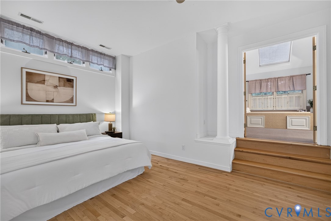 Room featuring wood-finish flooring, clerestory windows, a decorative column, and a raised platform entry with double doors