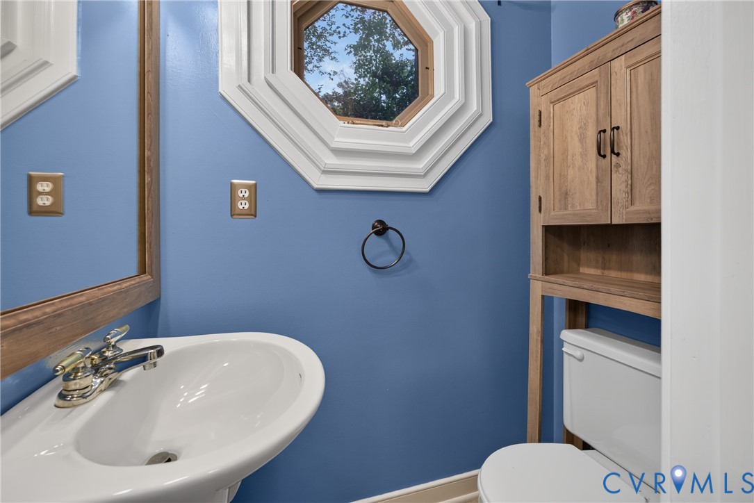 Octagonal window with custom molding, wall-mounted wood-finish cabinetry, porcelain pedestal sink, and polished metal hardware