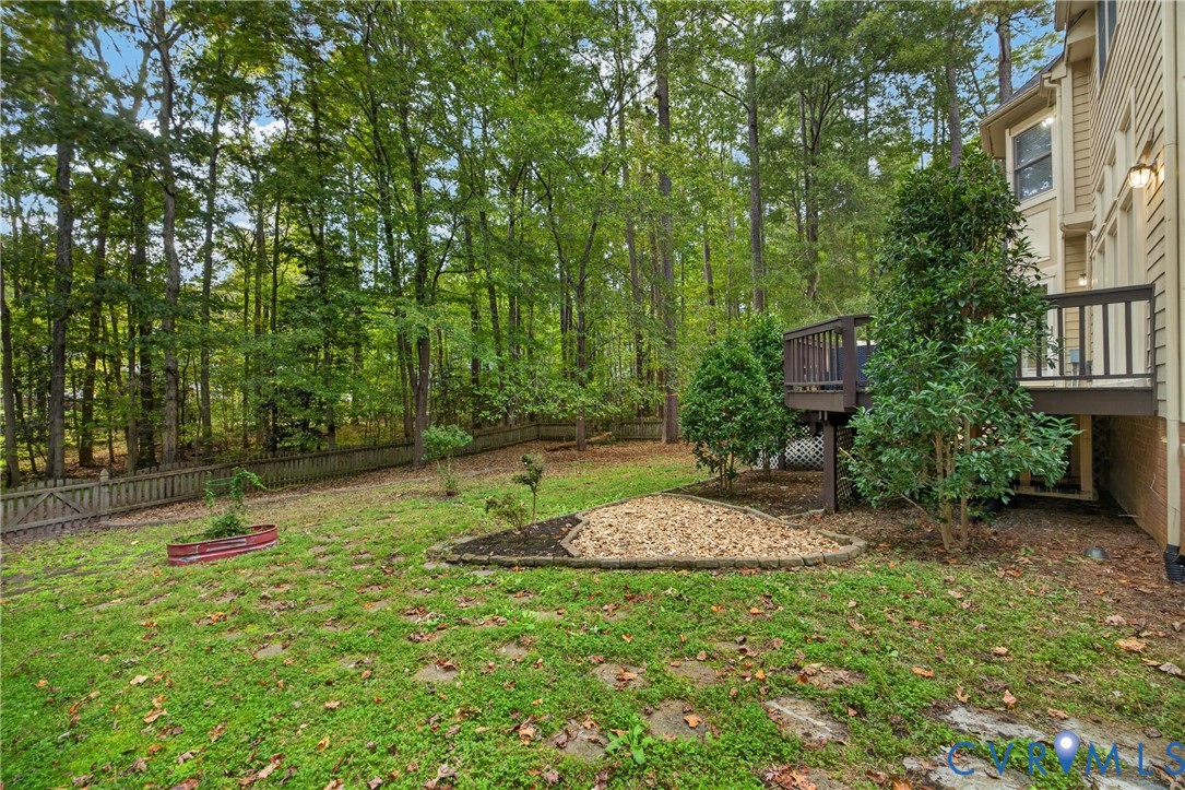 Backyard featuring a raised wooden deck, stone-bordered landscaping beds, a gravel garden area, and a perimeter fence, set against a backdrop of mature trees