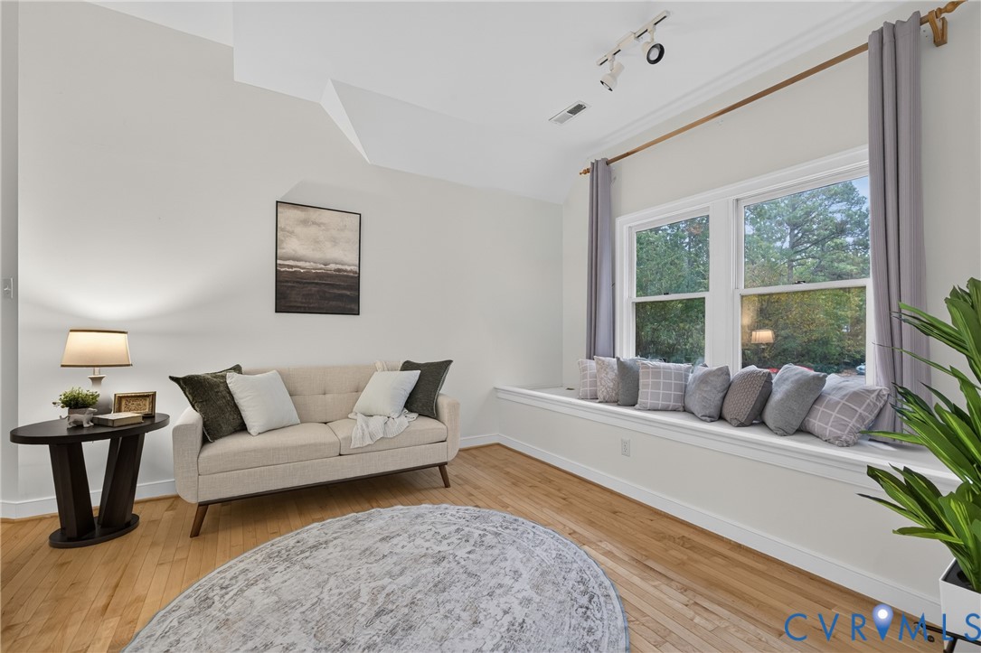 Vaulted ceiling, wood-finish flooring, and a built-in window seat featuring double-pane windows with integrated curtain rod