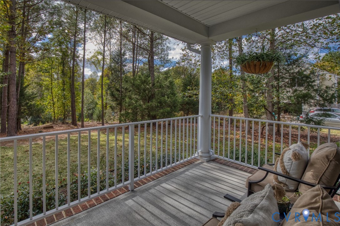 Covered porch featuring concrete flooring, a classic column, and white metal railing, opening to a wooded landscape