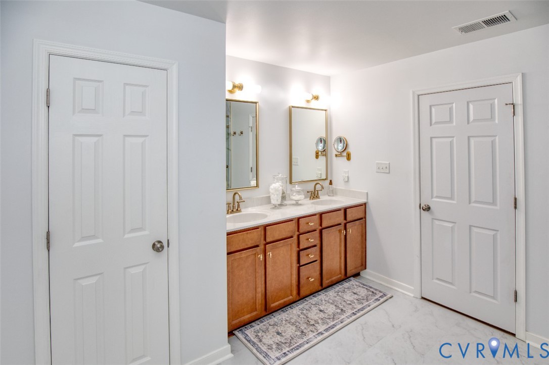 Dual-sink vanity with wood-finish cabinetry, solid surface countertop, metallic faucets, and wall-mounted mirrors