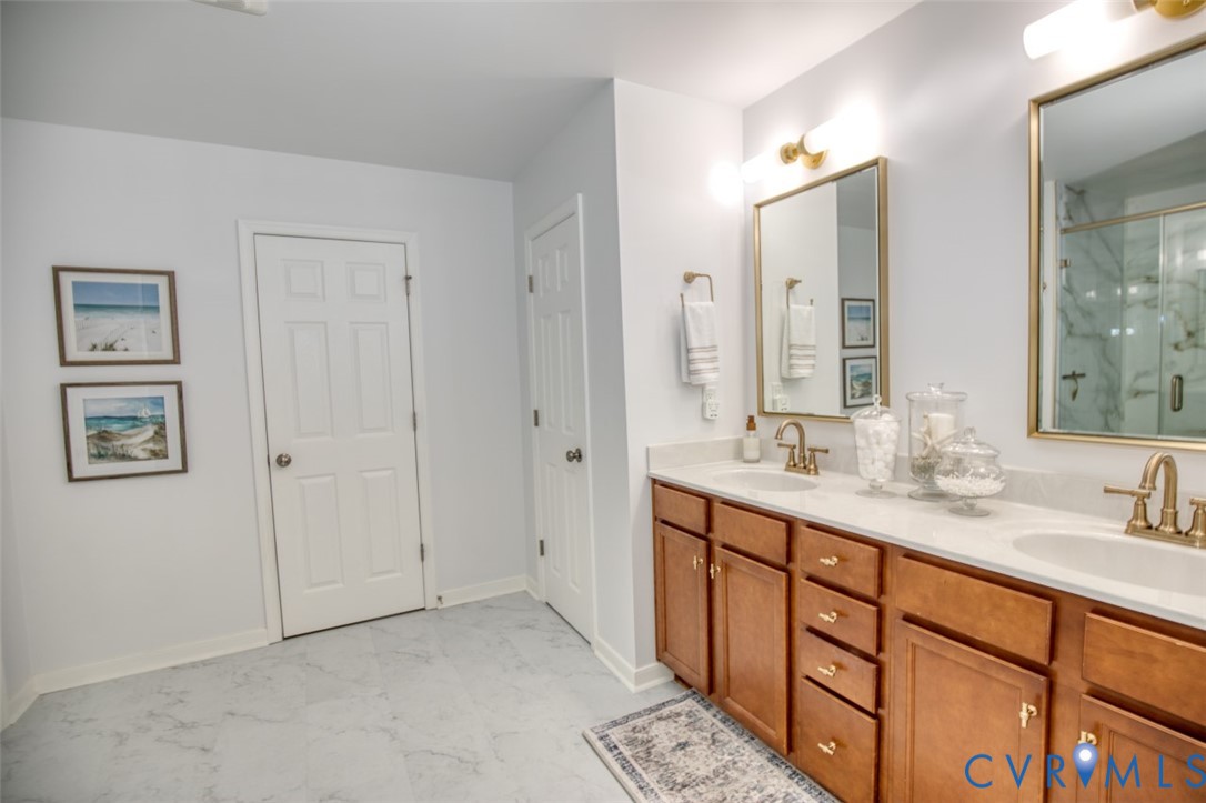 Dual-sink vanity with light stone countertop, brass-finish faucets, wood cabinetry, and individual wall-mounted mirrors