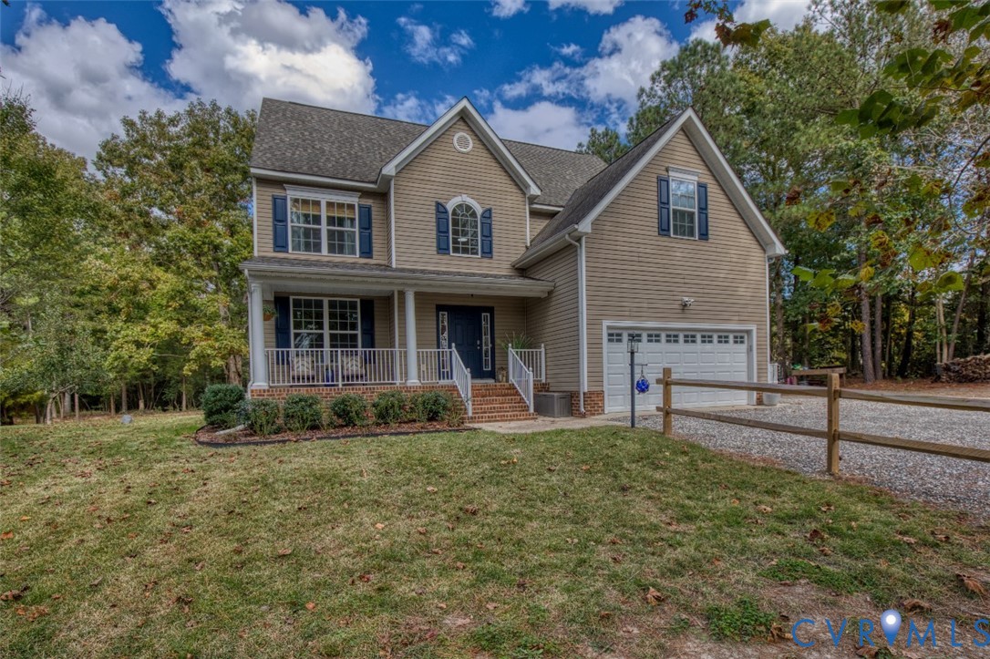 Two-story residence featuring horizontal siding, a covered front porch with white railing, brick-accented entryway, attached two-car garage, and wooden split-rail fencing Two-story residence featuring horizontal siding, a covered front porch with white railing, brick-accented entryway, attached two-car garage, and wooden split-rail fencing
