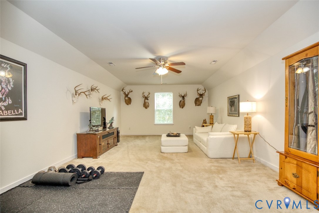 Spacious room featuring vaulted ceilings, neutral carpeting, and a central ceiling fan