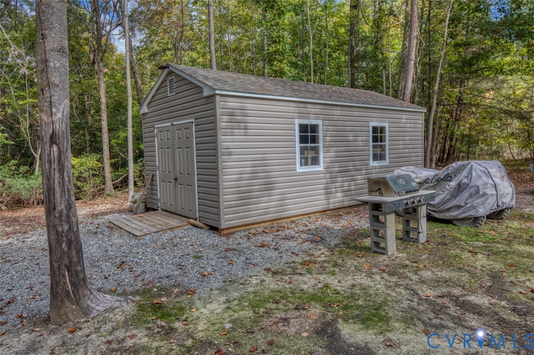 Detached storage structure featuring horizontal vinyl siding, a gabled roof, dual-entry doors, and multi-pane windows, situated on a gravel pad Detached storage structure featuring horizontal vinyl siding, a gabled roof, dual-entry doors, and multi-pane windows, situated on a gravel pad