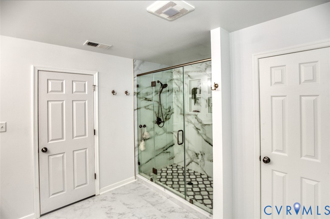 Walk-in glass shower enclosure featuring large-format stone-patterned wall tile, integrated recessed shelving, patterned tile flooring, and matte black hardware