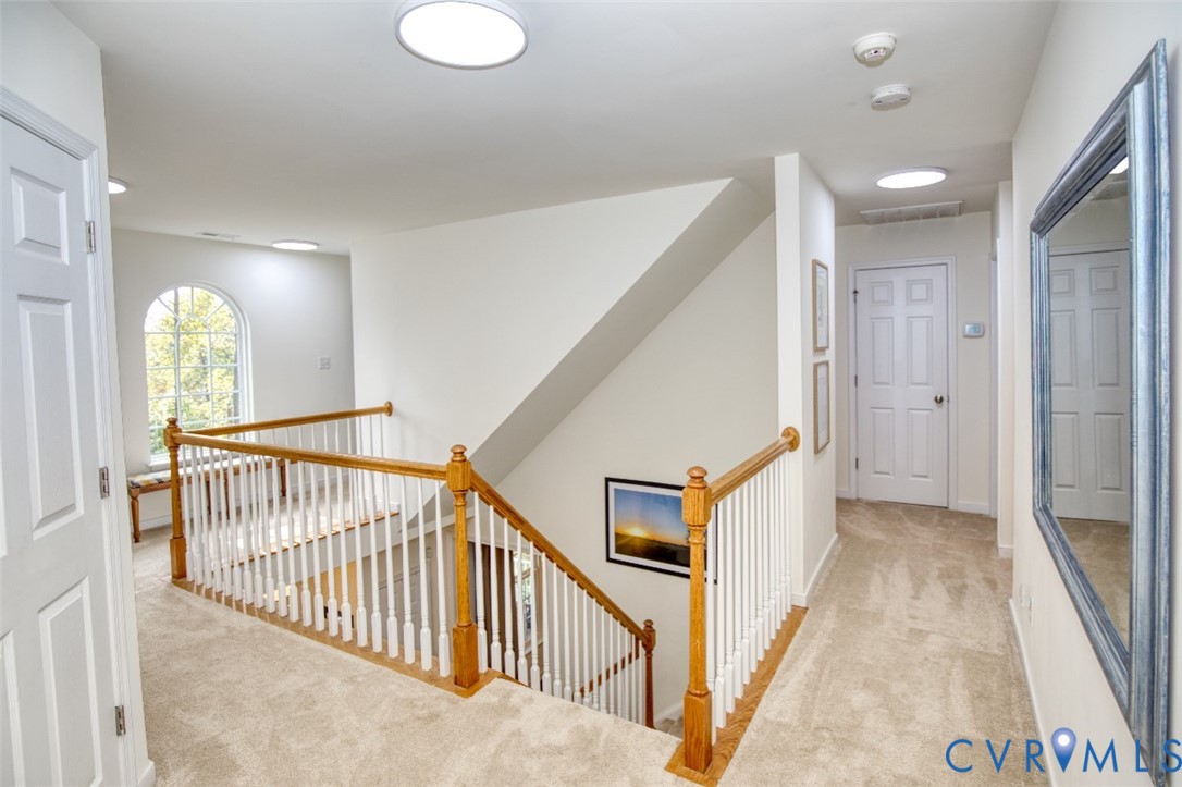Landing area featuring wall-to-wall carpeting, wood-finish handrails, white balusters, recessed lighting, and an arched window