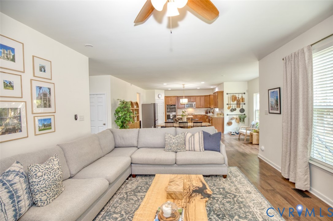 Wood-finish flooring, ceiling fan with light fixture, and kitchen featuring wood cabinetry and built-in appliances