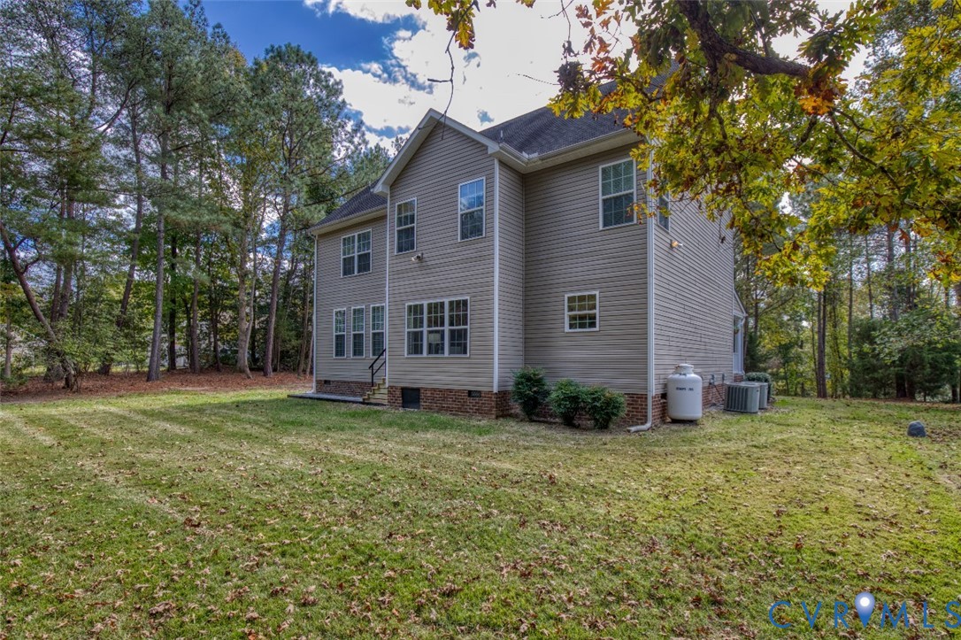 Two-story residence featuring light-colored horizontal siding, brick foundation detailing, multi-pane windows, and an expansive rear yard bordered by mature trees Two-story residence featuring light-colored horizontal siding, brick foundation detailing, multi-pane windows, and an expansive rear yard bordered by mature trees