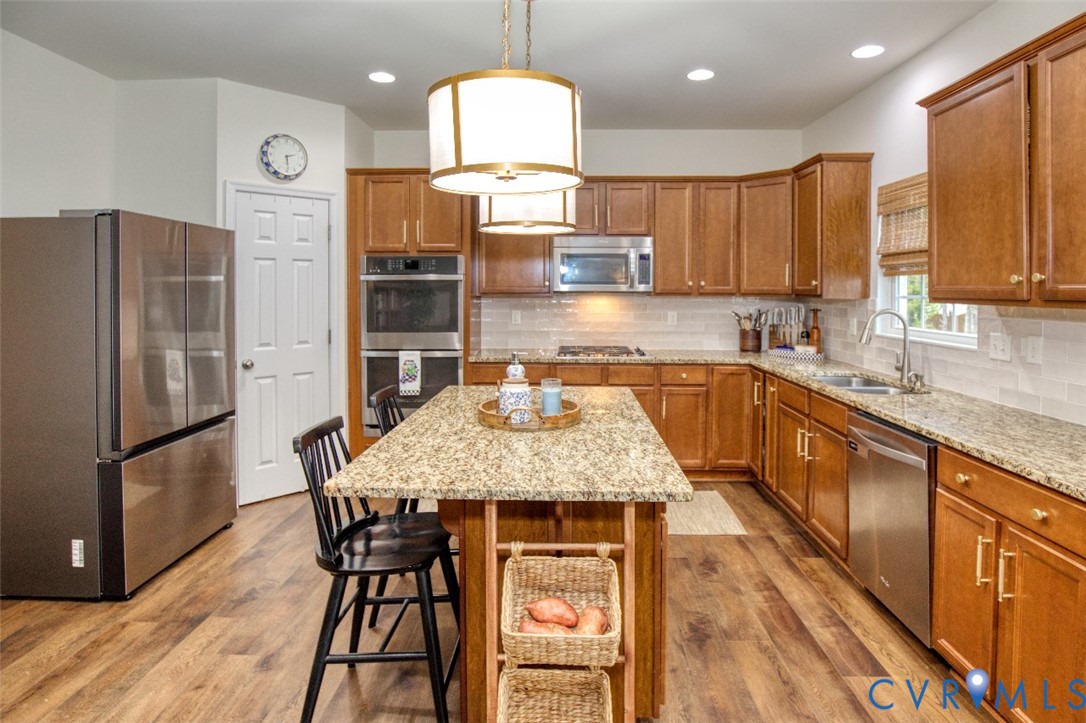 Kitchen featuring wood cabinetry, stone-surface countertops, wood-finish flooring, a central island, and stainless steel appliances
