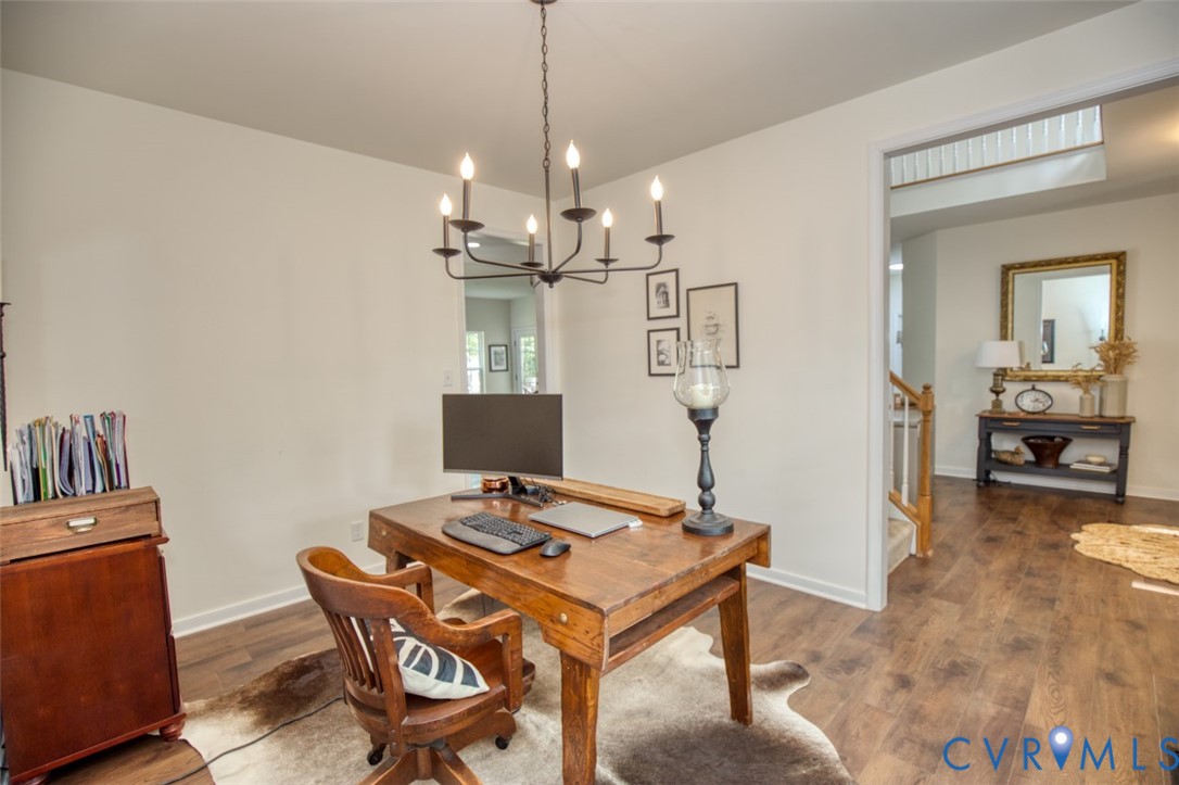Interior room featuring wood-finish flooring, a matte black metal candelabra-style chandelier, and a wood banister with white balusters