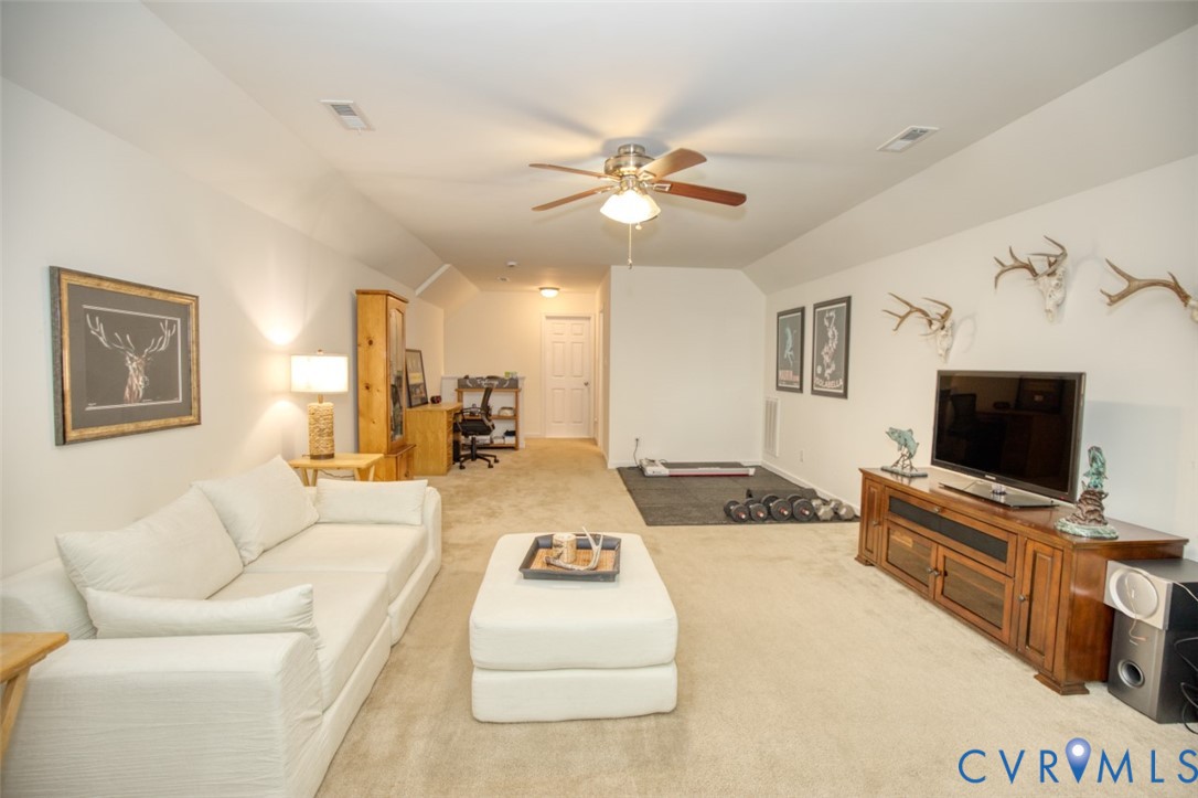 Neutral-toned interior space featuring carpeted flooring, a multi-blade ceiling fan, slanted ceiling architecture, and a central white six-panel door
