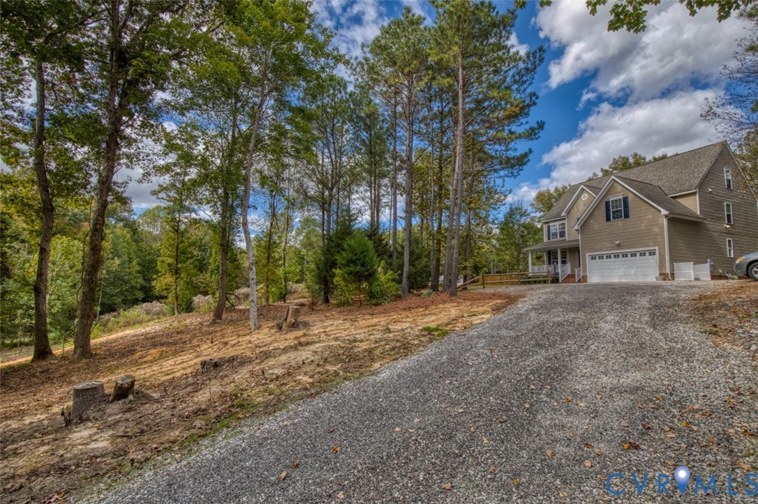 Multi-story residence featuring a shingled roof, neutral-toned siding, a two-car garage, and a private gravel driveway nestled within a wooded lot