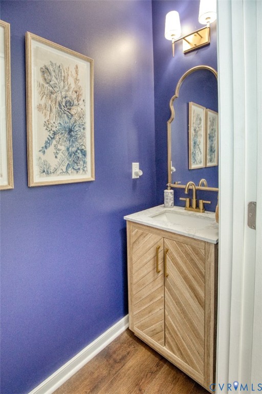 Custom wood-finish vanity with herringbone-patterned cabinetry, white stone-composite countertop, arched wall mirror, metallic finish faucet, and dual-shade wall sconce