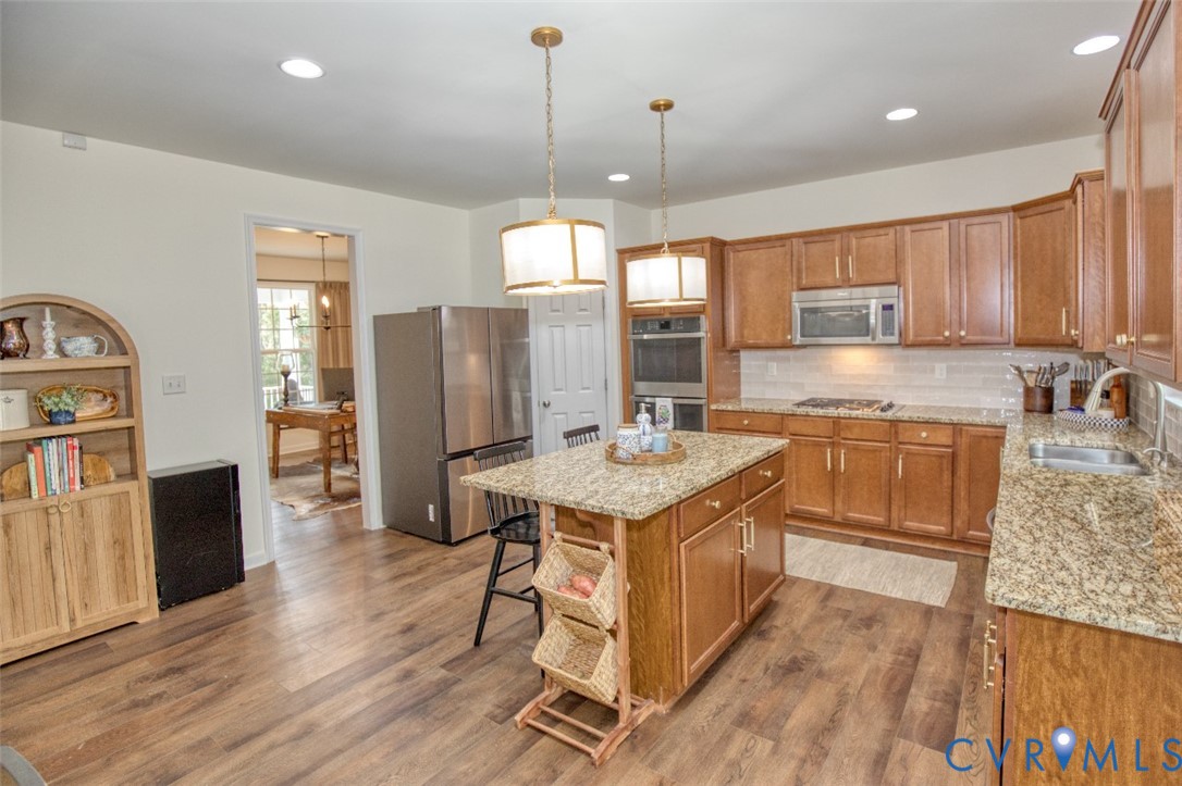 Kitchen featuring wood cabinetry, stone-finish countertops, stainless steel appliances, a central island, and wood-finish flooring