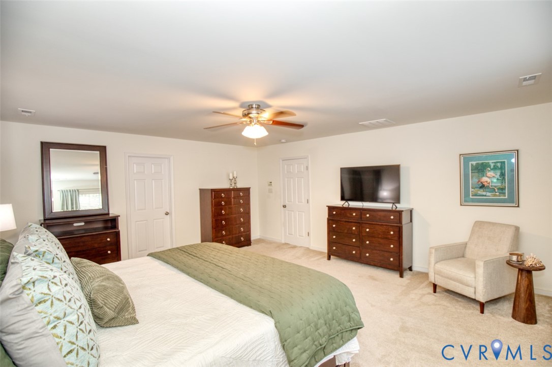 Neutral-toned carpeted flooring, multi-panel interior doors, and a central ceiling fan with integrated lighting