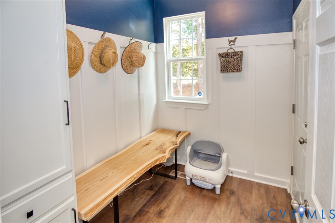 Mudroom area featuring white vertical wall paneling, built-in cabinetry, wood-finish flooring, and a live-edge wood bench with a metal frame