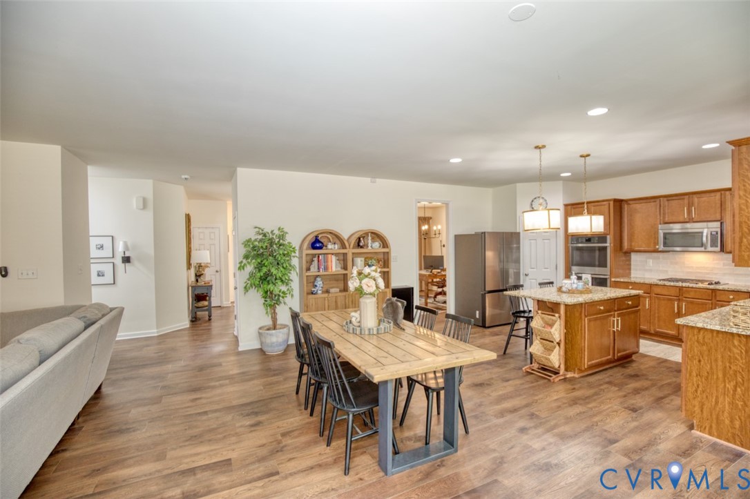 Kitchen featuring wood cabinetry, stone countertops, a center island with pendant lighting, and stainless steel appliances, all set over wood-finish flooring