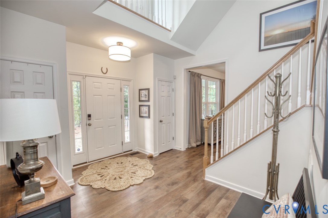 Foyer featuring double-height ceilings, wood-finish flooring, a drum-style pendant light, and a staircase with a wooden handrail and white balusters