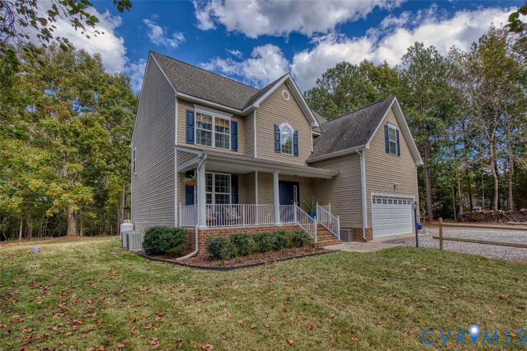 Two-story residence featuring light-toned horizontal siding, brick foundation accents, a covered front porch with white railing, and an attached two-car garage Two-story residence featuring light-toned horizontal siding, brick foundation accents, a covered front porch with white railing, and an attached two-car garage