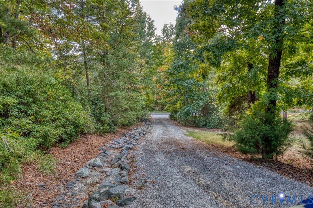 Gravel driveway bordered by stone landscaping and mature wooded foliage