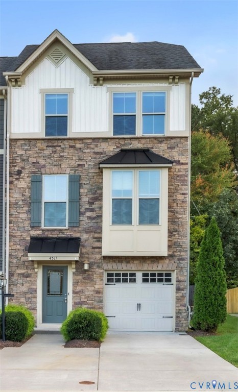 Three-story exterior featuring multi-toned stone masonry, vertical board-and-batten siding, a metal-accented bay window, and a carriage-style garage door