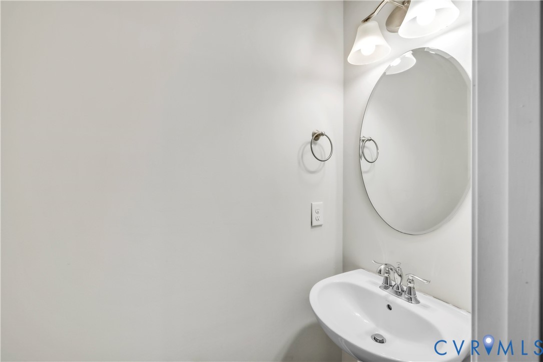 Wall-mounted oval mirror, pedestal sink with chrome dual-handle faucet, and three-light vanity fixture