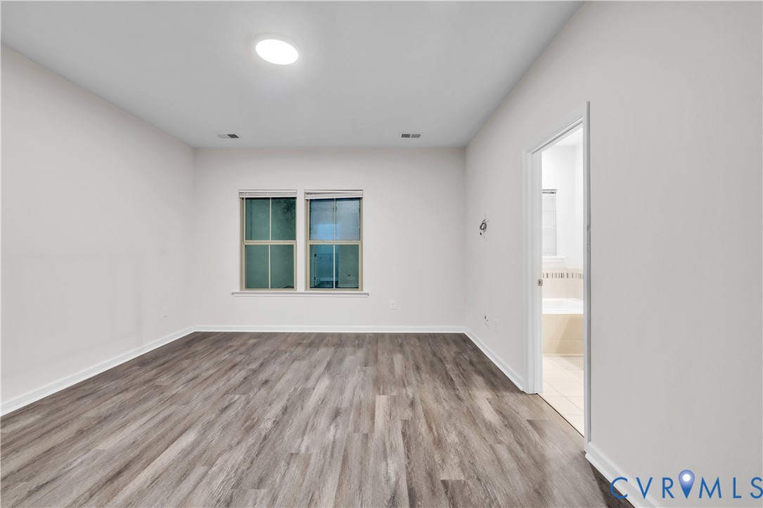 Spacious room featuring wood-finish flooring, neutral wall tones, dual-pane windows, and a ceiling-mounted light fixture