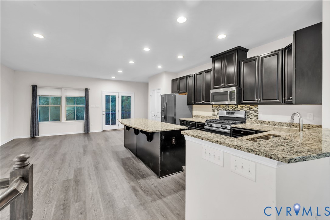 Kitchen featuring dark cabinetry, stone countertops, integrated stainless steel appliances, a center island with seating space, and wood-finish flooring