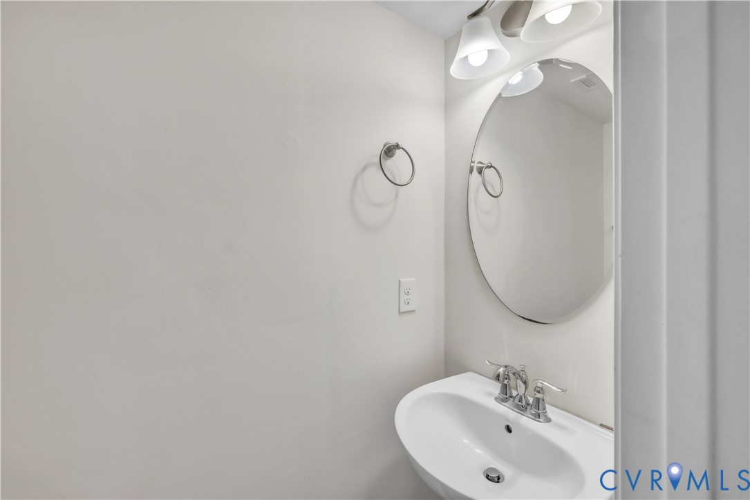 Oval wall-mounted mirror featuring a polished metal finish, pedestal sink with a dual-handle chrome faucet, and multi-bulb vanity light fixture Oval wall-mounted mirror featuring a polished metal finish, pedestal sink with a dual-handle chrome faucet, and multi-bulb vanity light fixture