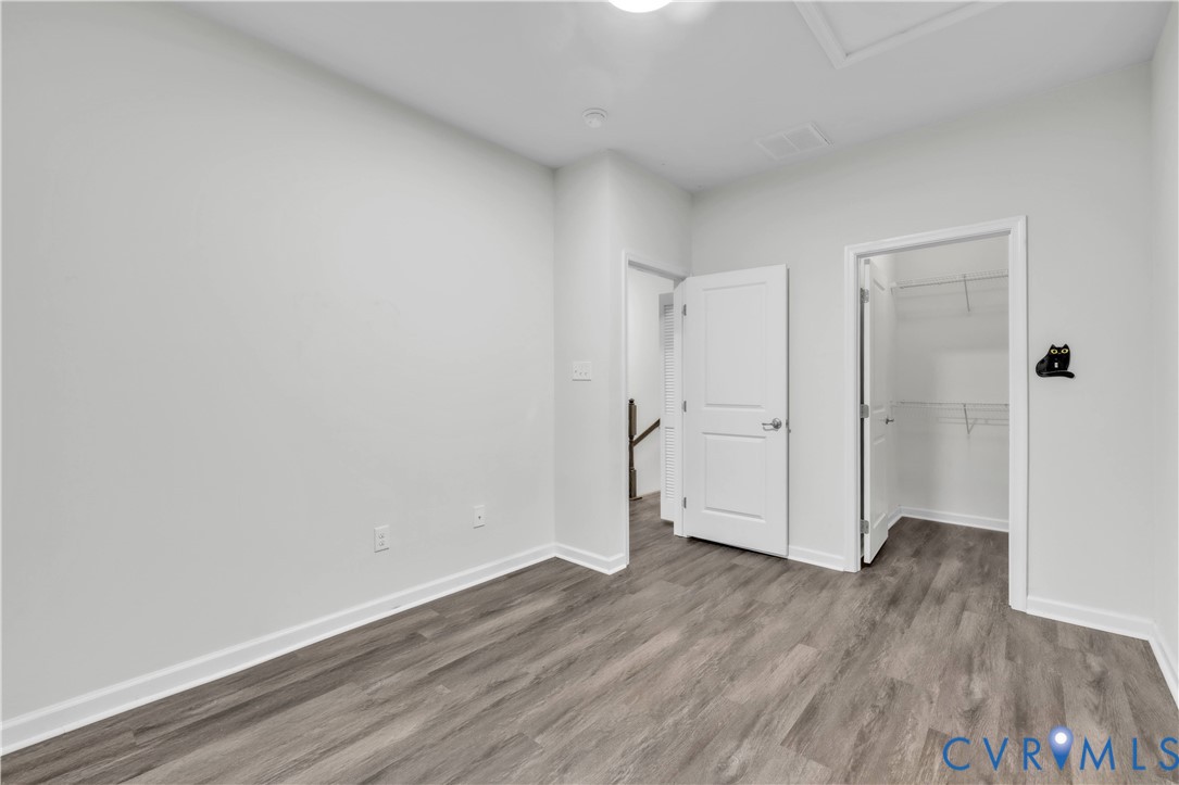 Room with neutral wall tones, wood-finish flooring, and a walk-in closet featuring built-in wire shelving