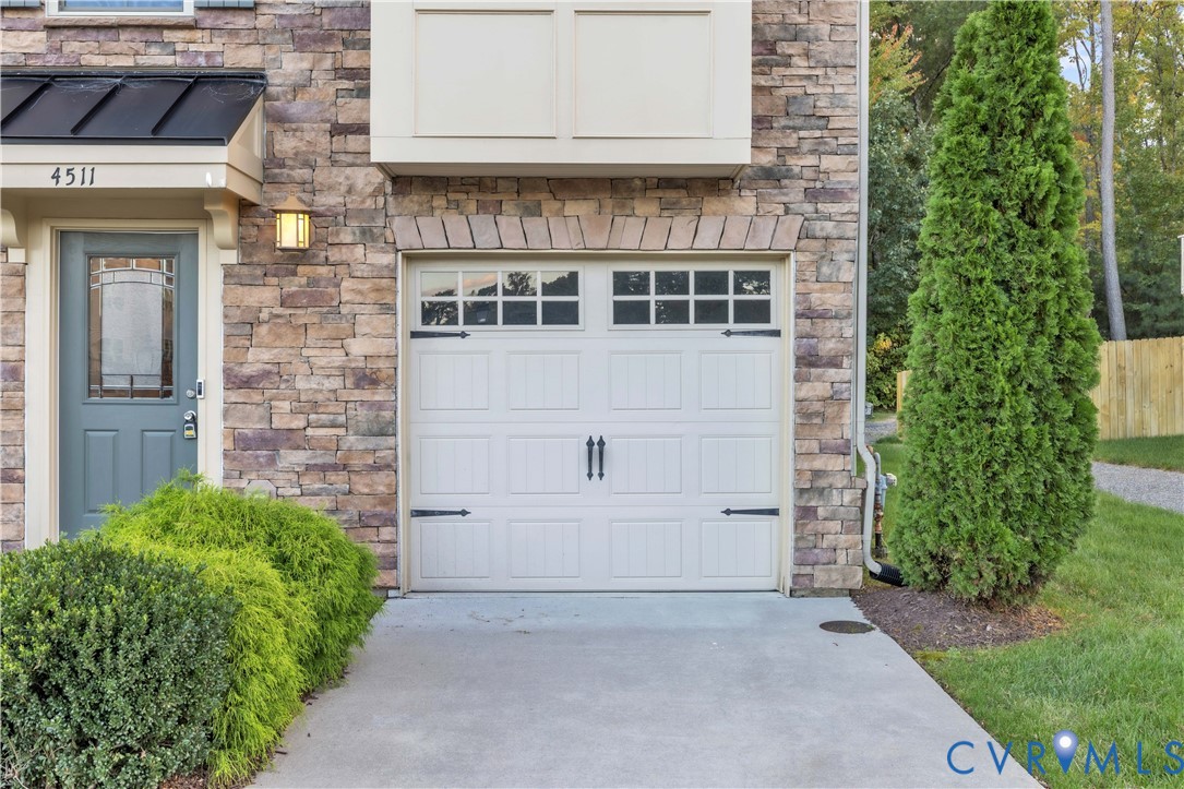 Exterior faade featuring stone veneer siding, an attached garage with window-pane detailing and decorative hardware, a metal roof accent, and a solid entry door with a glass insert Exterior faade featuring stone veneer siding, an attached garage with window-pane detailing and decorative hardware, a metal roof accent, and a solid entry door with a glass insert
