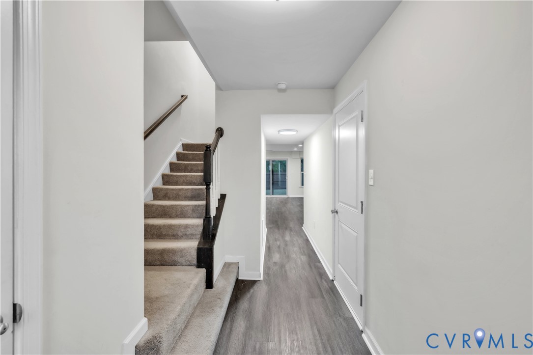 Staircase featuring carpeted steps, a dark-stained wood handrail, and a white baluster, finished with wood-finish flooring and a white paneled door