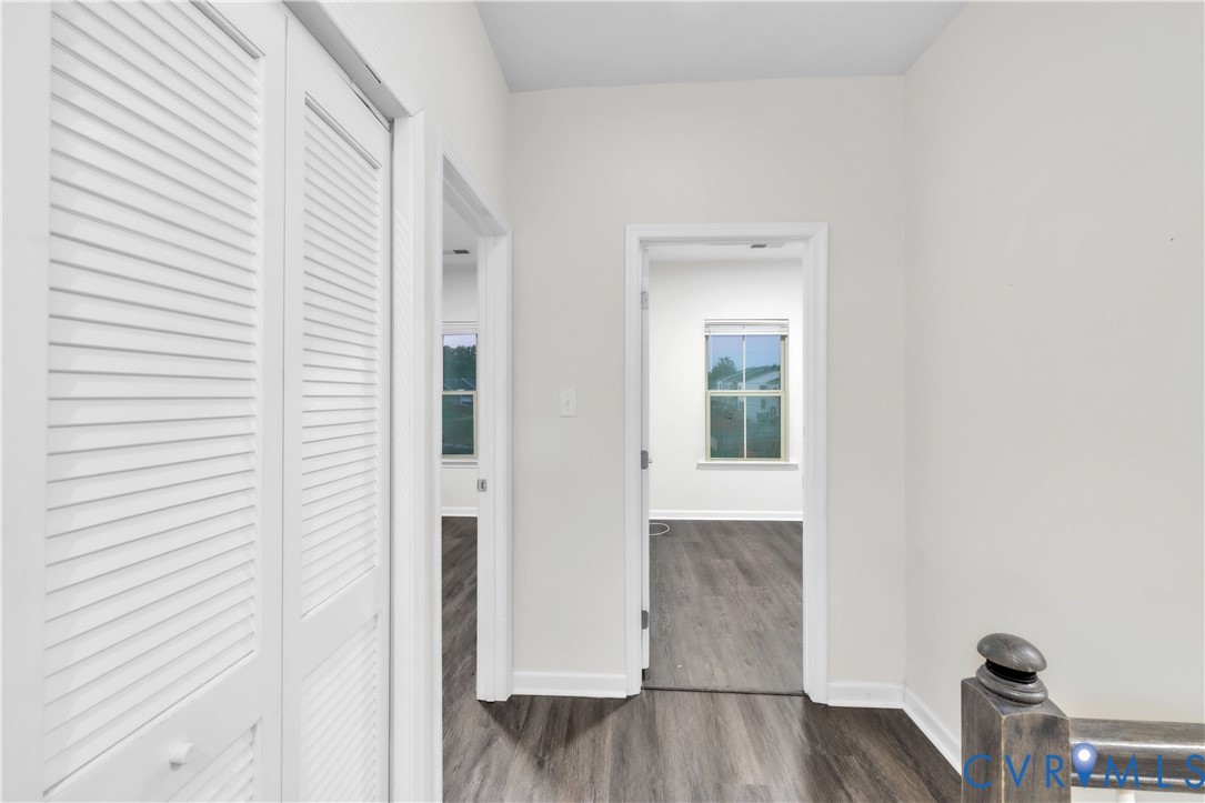 Hallway featuring wood-finish flooring, white louvered closet doors, and dark-toned baluster