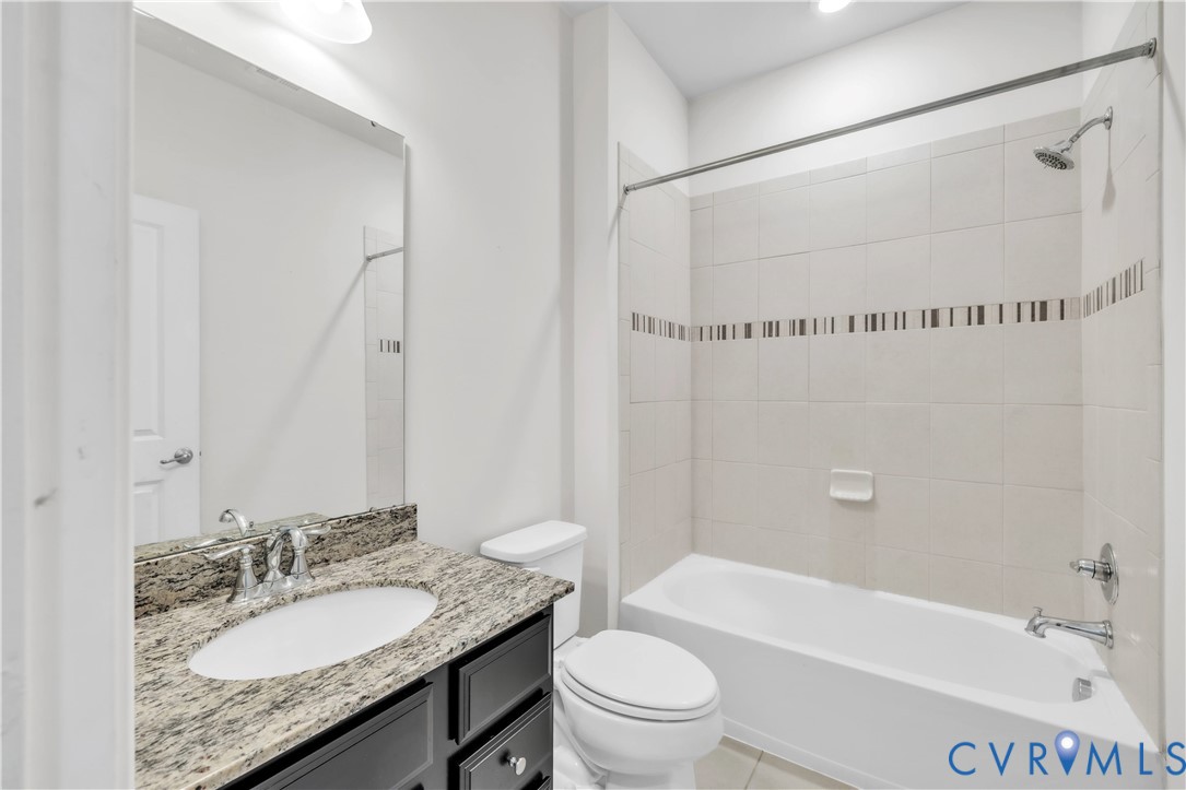 Bathroom featuring a dark wood-finish vanity, stone-patterned countertop, oval under-mount sink, and a shower-tub combination with decorative tile inlay