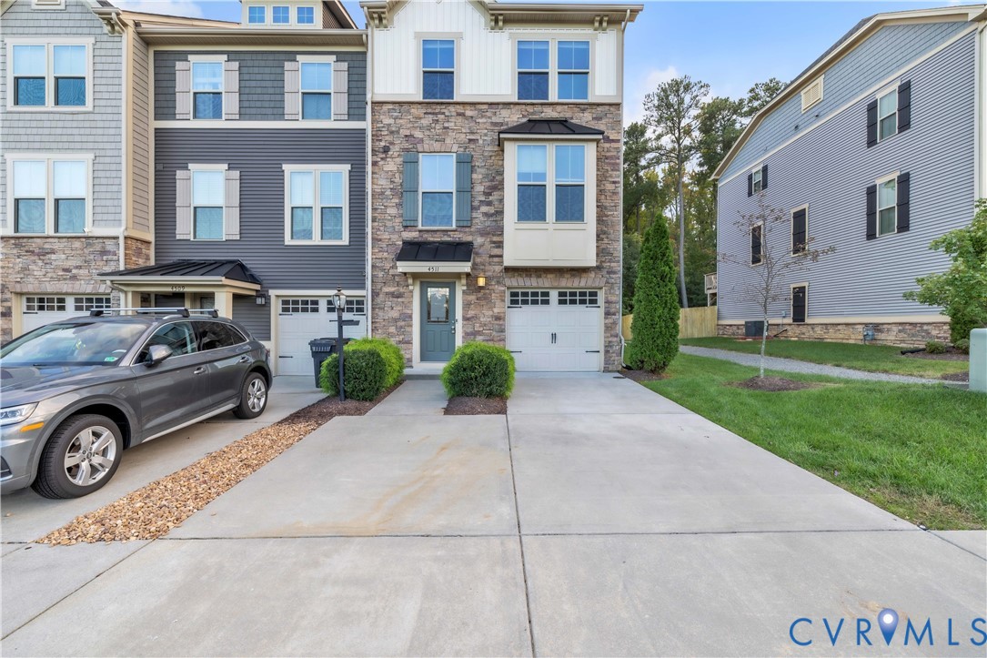 Three-story townhome exterior featuring stone veneer facade, vertical board-and-batten siding, metal roof accents, and concrete driveway Three-story townhome exterior featuring stone veneer facade, vertical board-and-batten siding, metal roof accents, and concrete driveway