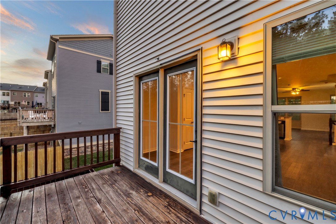 Exterior deck featuring wood-plank flooring, a wood railing, dual glass-panel doors, and wall-mounted exterior lighting