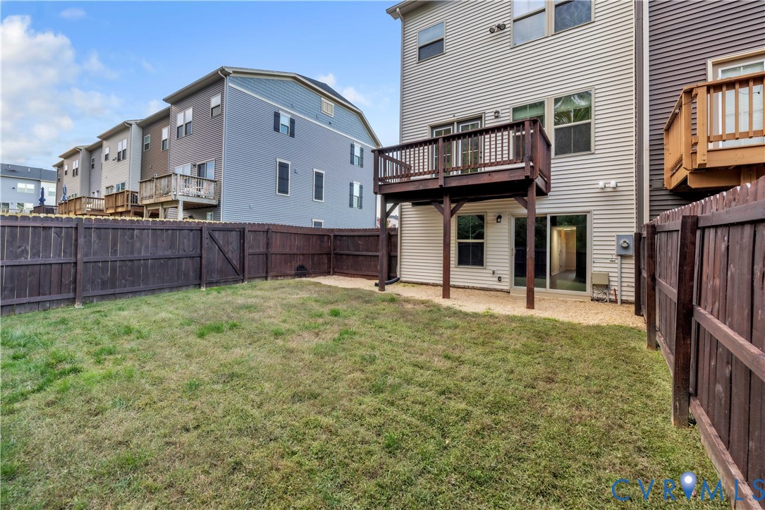 Rear yard featuring a grass lawn, gravel patio area, elevated wood deck, and wood privacy fencing