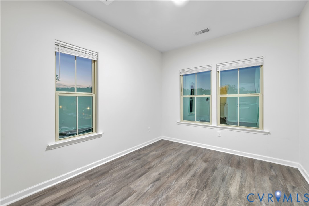 Room featuring wood-finish flooring, neutral walls, and three double-hung windows with installed blinds