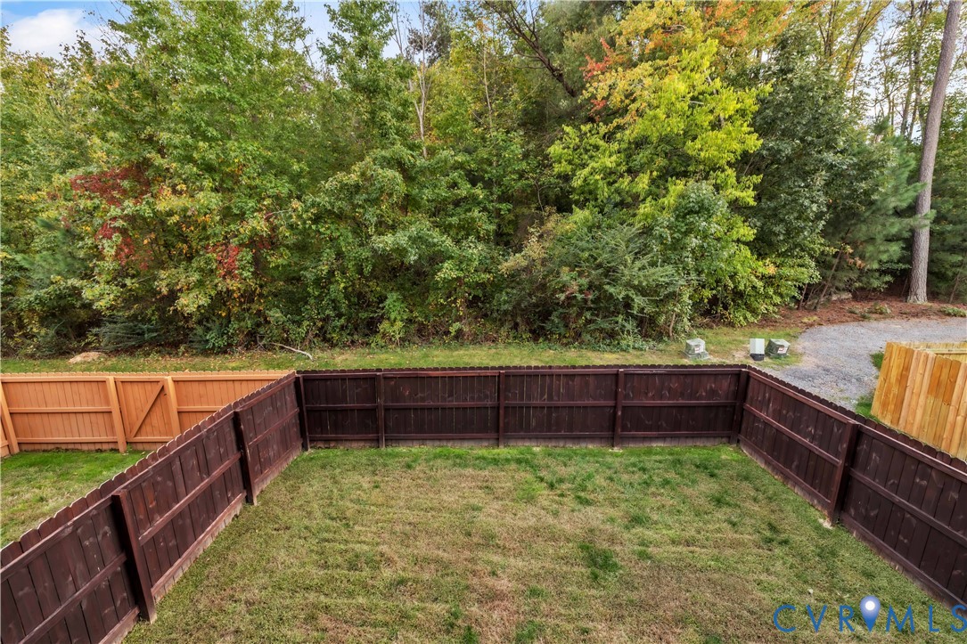 Rear yard enclosed by dark-stained wood privacy fencing, featuring a grass lawn and direct border to dense mature tree lines