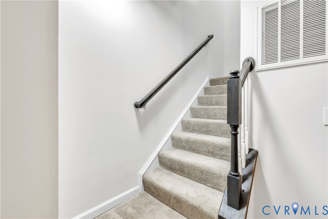 Staircase featuring wall-to-wall carpeting, a dark-finish wood handrail, a matching dark-finish newel post, and white balusters