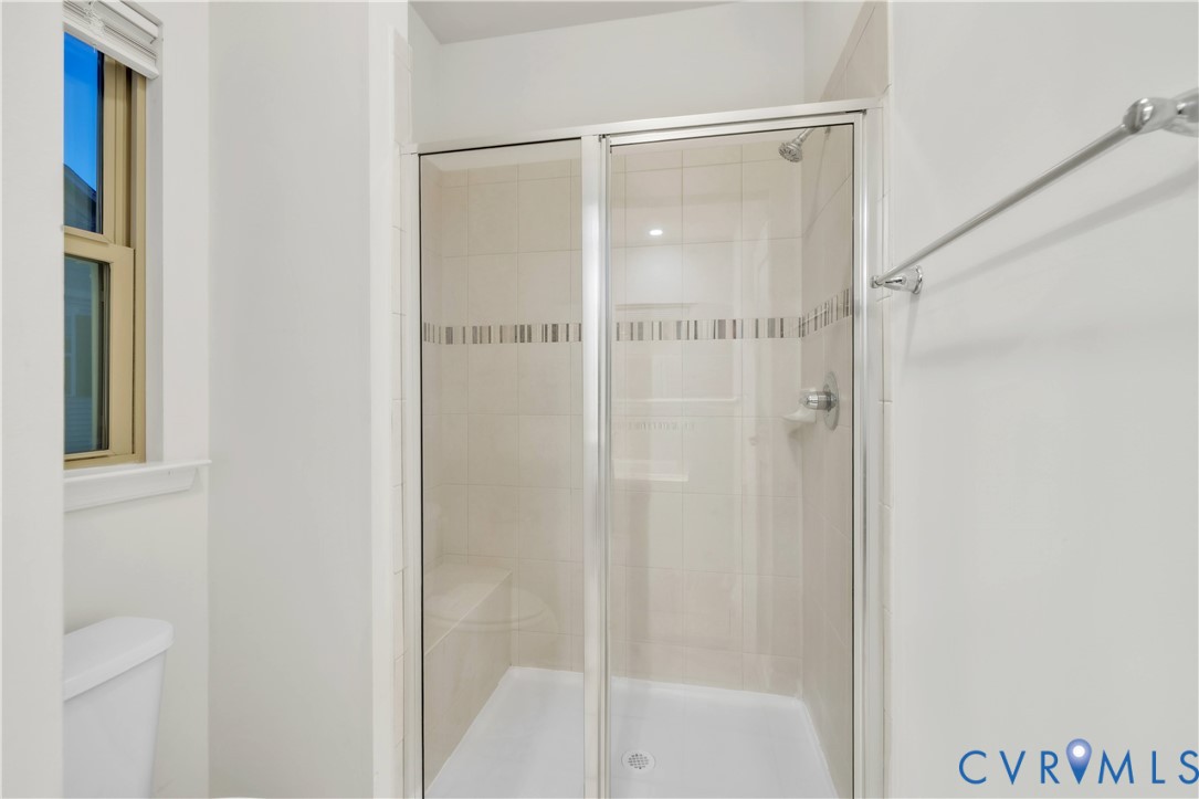 Walk-in shower featuring a glass sliding enclosure, tile wall surround with decorative inlay, built-in bench seating, and polished metal fixtures