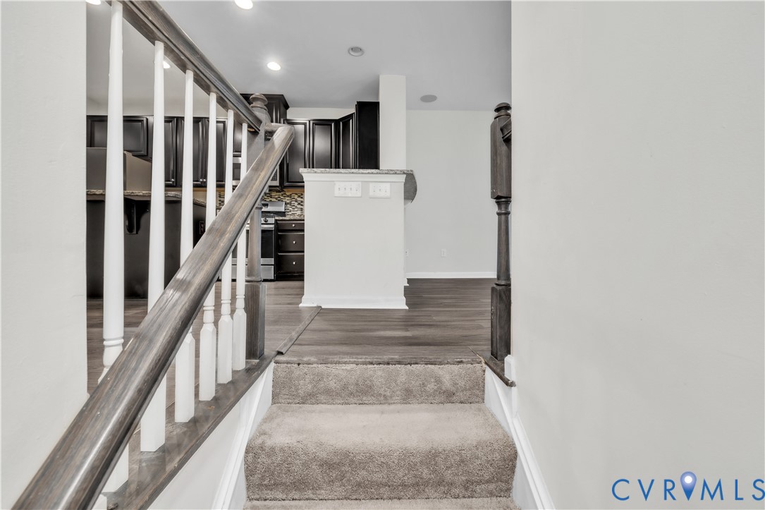 Staircase featuring carpeted treads, wood-finish handrail, and white balusters