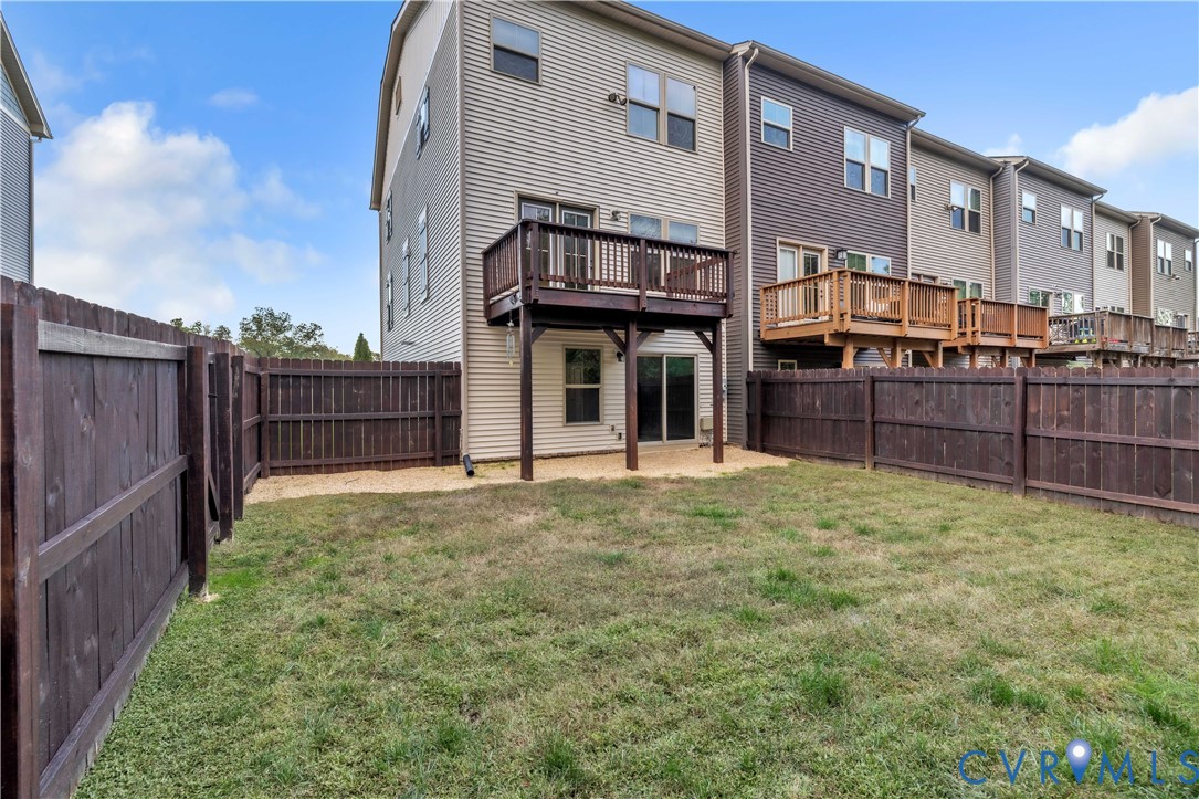 Rear exterior featuring a wood-plank deck, sliding glass door, and a private, fully fenced backyard